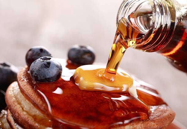 Close-up of pouring maple syrup on stack of pancakes.